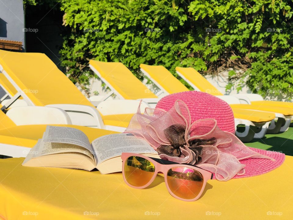 Pink sunglasses and a hat placed on a yellow sunbed with many yellow sunbeds in the background