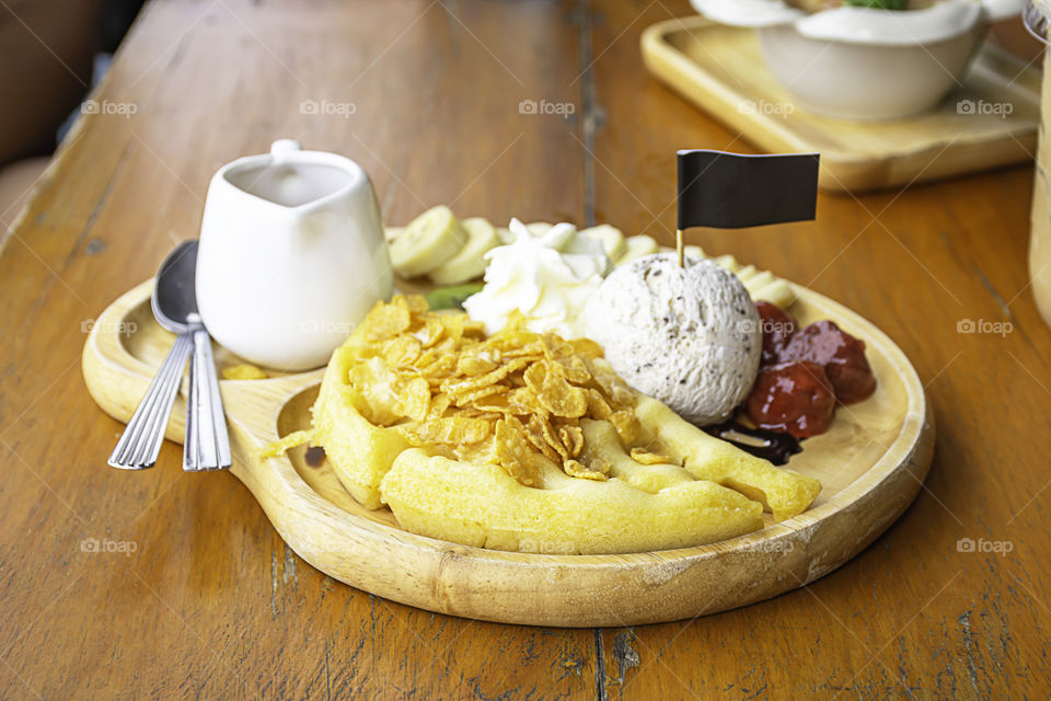 Sweet water pour on the waffle with ice cream and fruits including bananas, kiwi and strawberries in wooden plate on table.