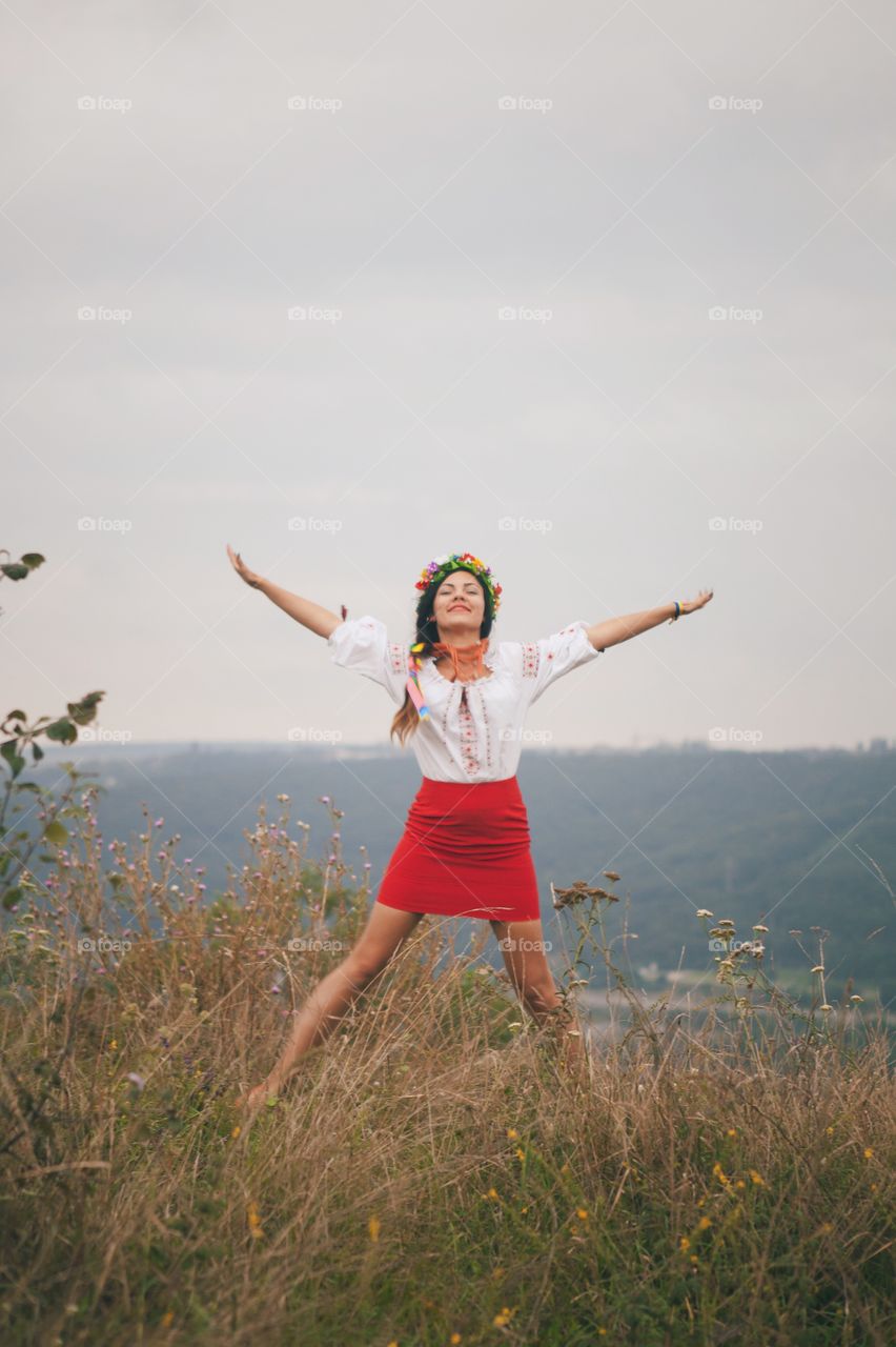 Smiling beautiful woman with arms raised and standing in front of mountain