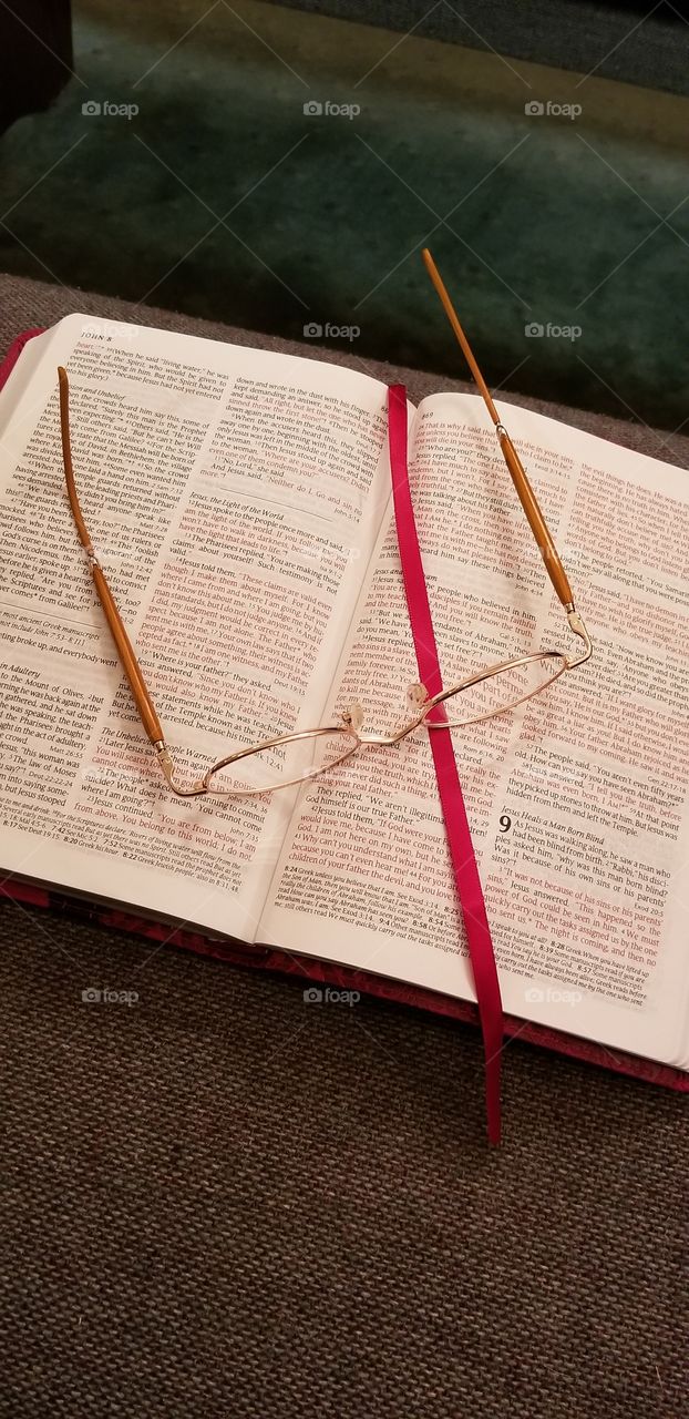 Reading glasses lying on a bible open to the book of John, lying on a pew in a church with the bookmark lying across the page.