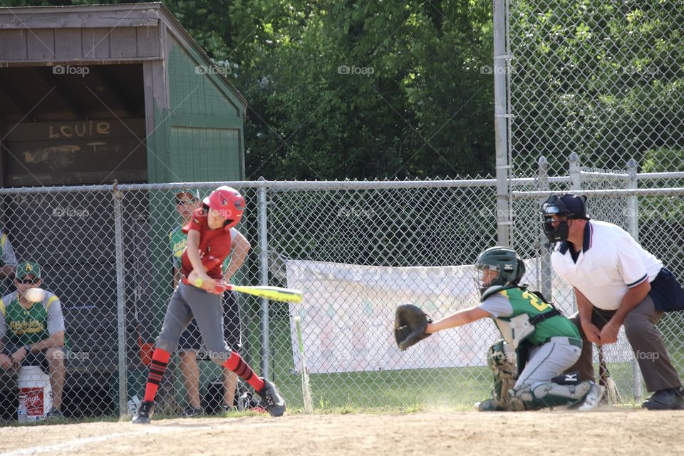 Baseball player swinging at pitch with catcher and umpire behind home plate