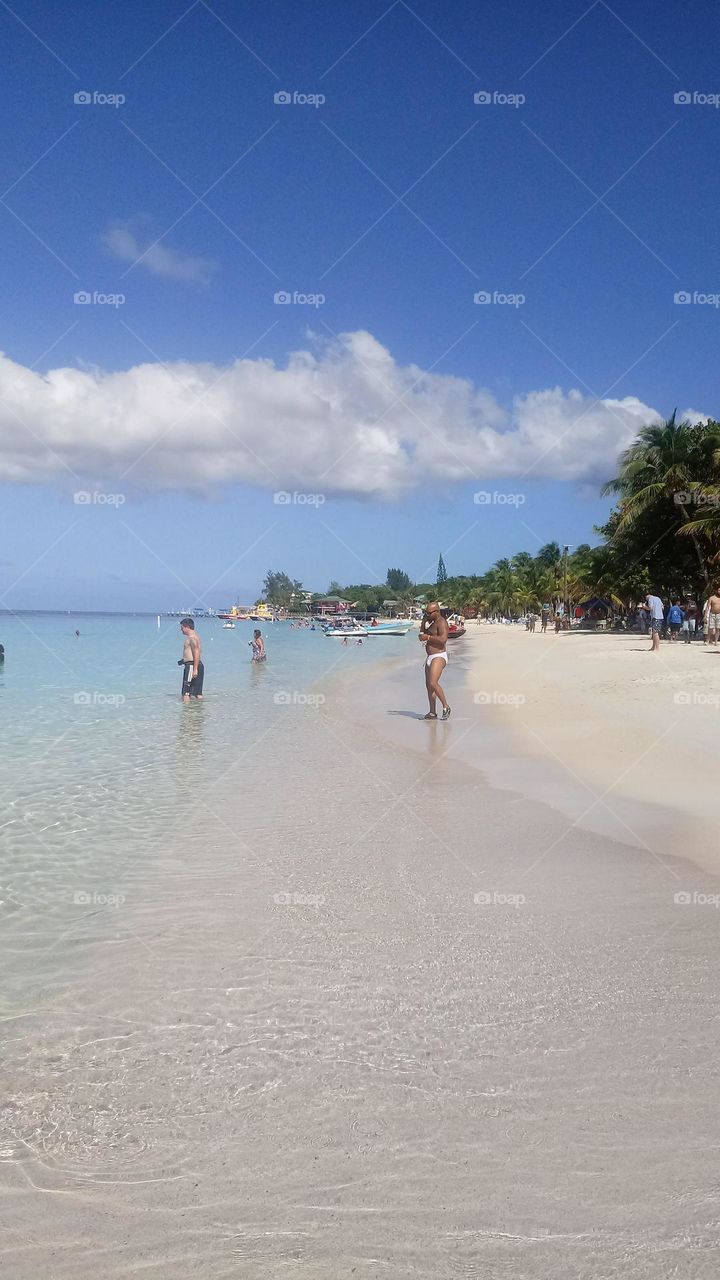 Beaches of Belize, clear waters, white sand beaches,  palm trees and a few people and big blue skys and clouds 