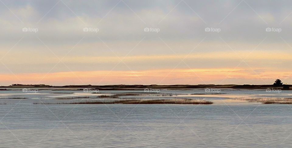 Peeks of sunlight peek through thick, grey winter clouds over high tide in the marsh 