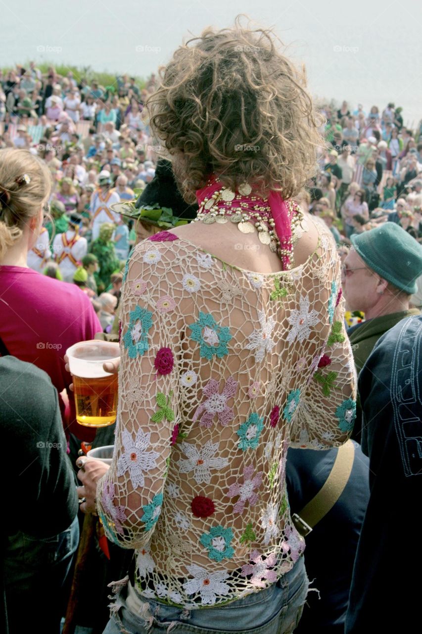 A man in a fabulous crocheted top stands within a large crowd at an outdoor summer event