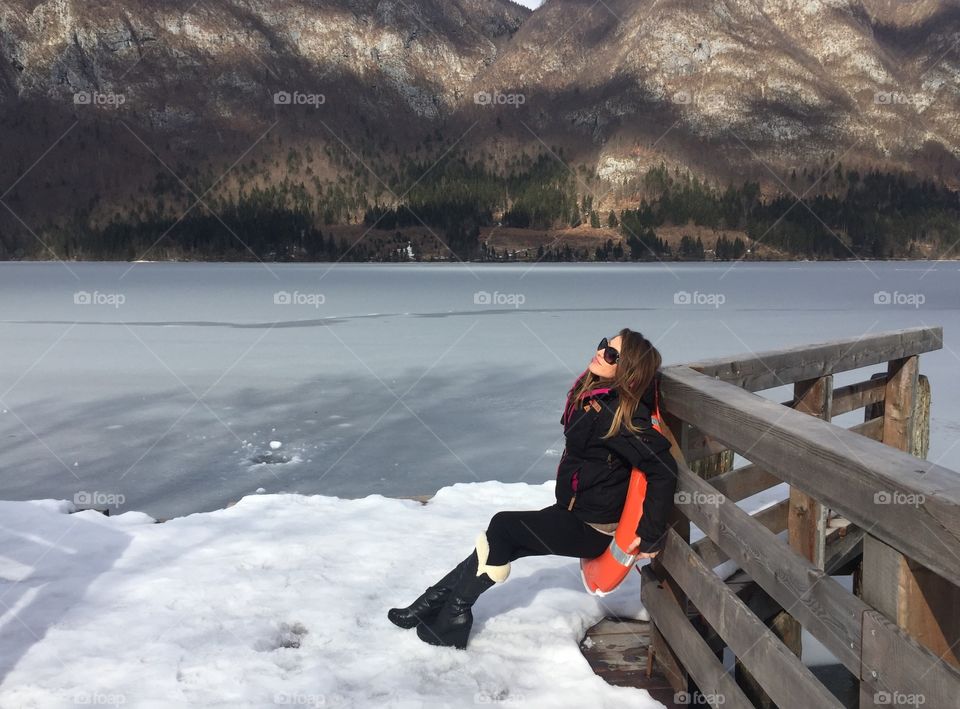 Woman sitting on lifebelt near frozen lake