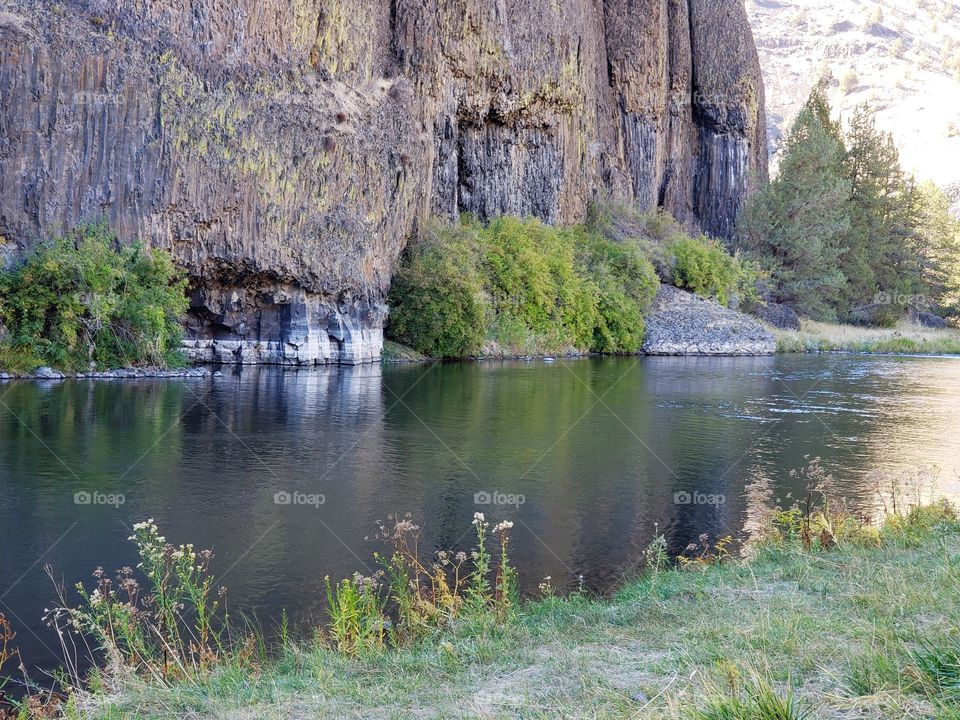 The beautiful Crooked River with fall colored bushes on its banks flows through a canyon formed from andesite and basalt flows on a nice autumn evening in Central Oregon. 