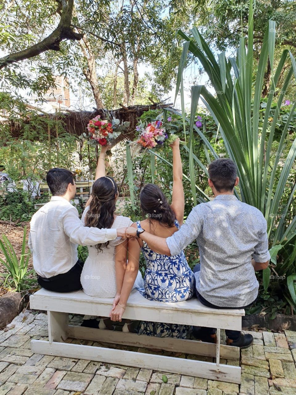 Married! Happiness doesn't need to be seen through the smile, but through body language. Two couples happily married sitting on a bench in the middle of nature
