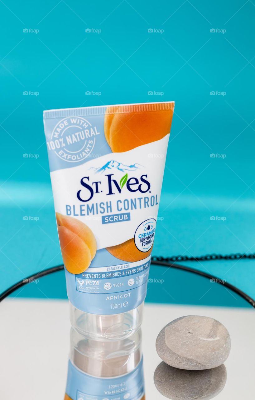 One tube of natural apricot scrub brand st. Ives with one stone stands on a round mirror with a black border and a chain reflected in it, side view close-up. Female cosmetics concept, body tie, beauty.