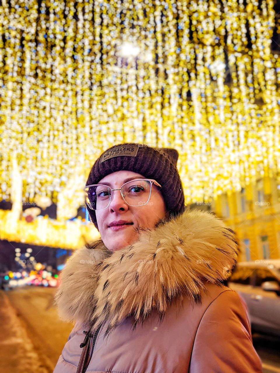 Portrait of young happy, beautiful woman in eye glasses in Christmas,  New Year city with illumination and garlands.