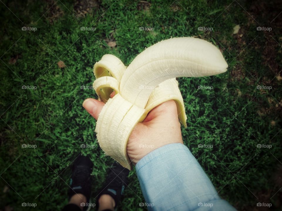 staying in good shape a woman holding a peeled banana in grass wearing running shoes