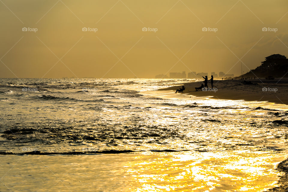 Sunset at Miami Beach, Florida. Sunlight reflecting from the ocean with orange and yellow skies while people are fishing at the beach. 