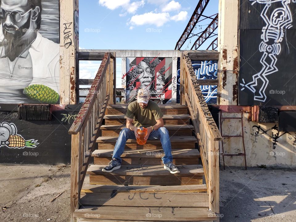 A man sitting on wood stairs at an abandoned urban outdoor art gallery.