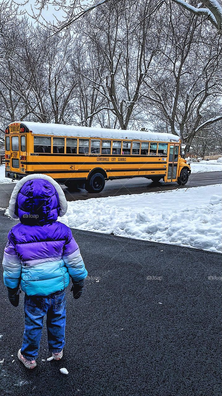 Toddler watches yellow school bus, yellow colored school bus passes by, yellow school bus in the neighborhood, toddler girl watches school bus, school bus driving through neighborhood, school bus makes stops in a community, curious toddler watching