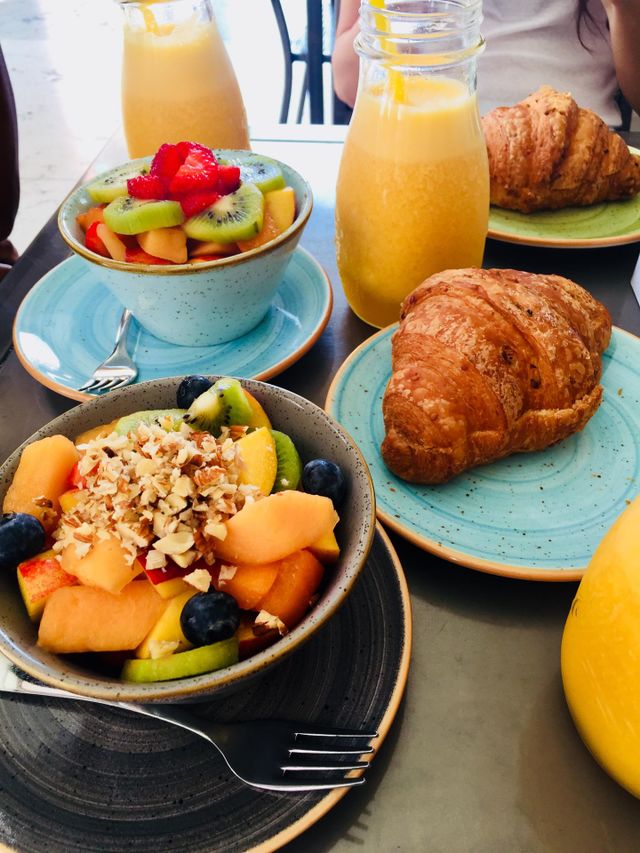 Healthy, bright and colorful breakfast served on ceramic colorful dishes and bowls, fruit salads, fruit fresh juices and  whole wheat croissants 