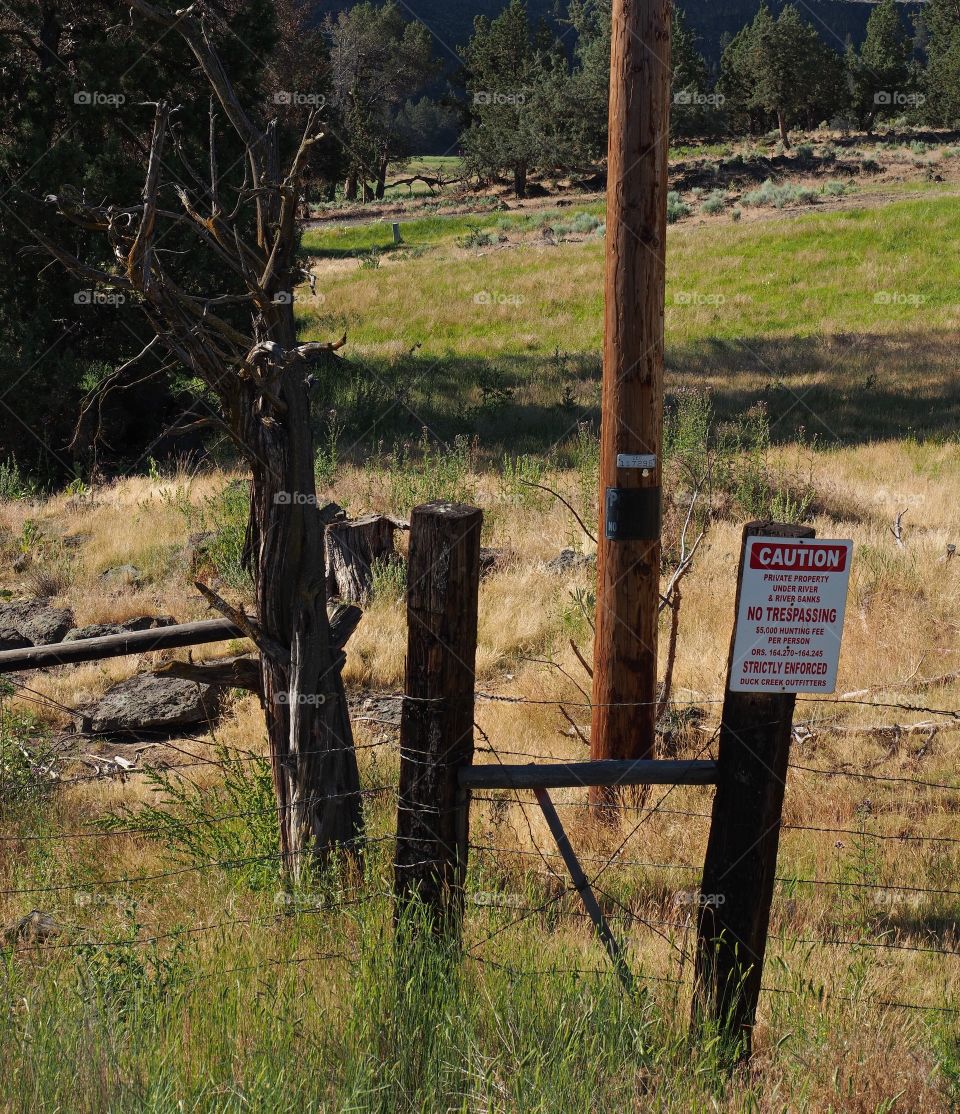 Fence posts with “No Trespassing” sign an a telephone pole with an old juniper tree snag in rural Central Oregon. 