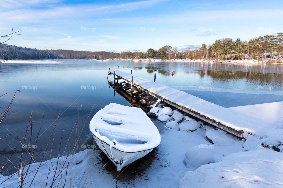 Boat and wooden pier by the lake covered in fresh snow on a beautiful winter day 