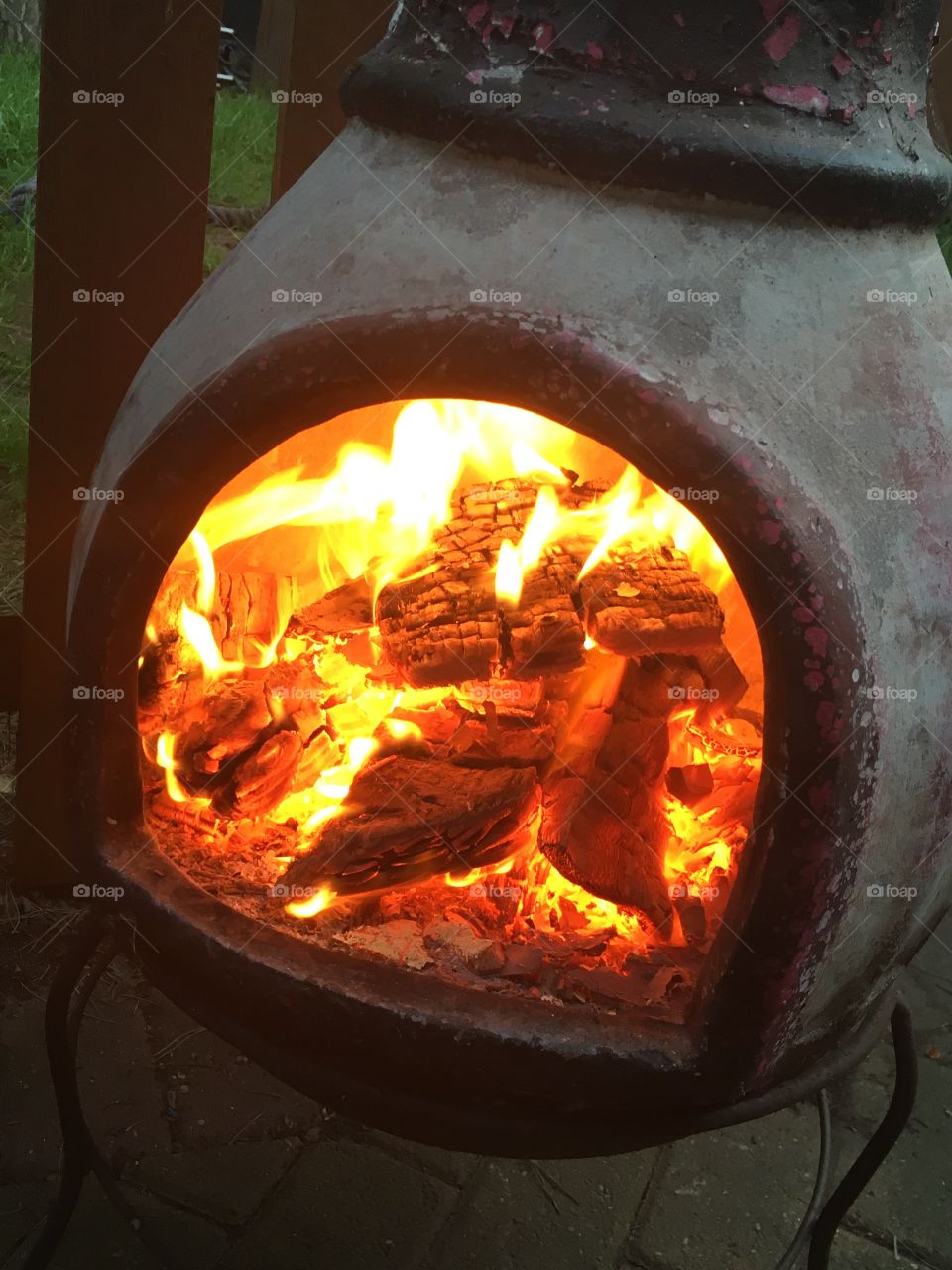 Chiminea burner with firewood logs inside burning, giving off a lot of heat in the garden 