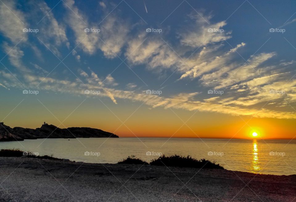 Beautiful feathery encrustations stretching diagonally across the entire sky with the sun setting over the horizon on the Mediterranean Sea of the island of Frioul in France, side view, close-up. Concept beautiful sky wallpaper.
