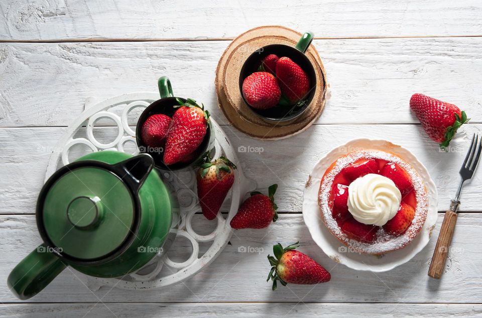 still life colorful food, sweet strawberry cake decorated with cream on a plate, green porcelain service with a cup of tea, homemade cakes