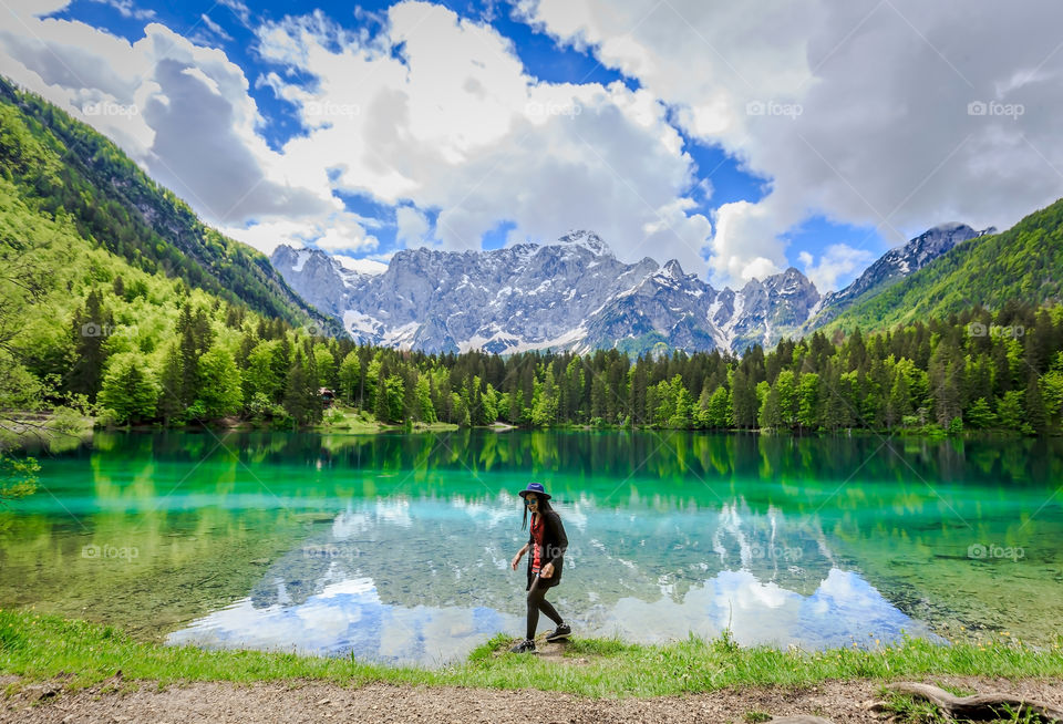 Female traveler enjoying by beautiful lake with turquoise color of water and stunning mountains on background on a beautiful bright sunnyday in spring 