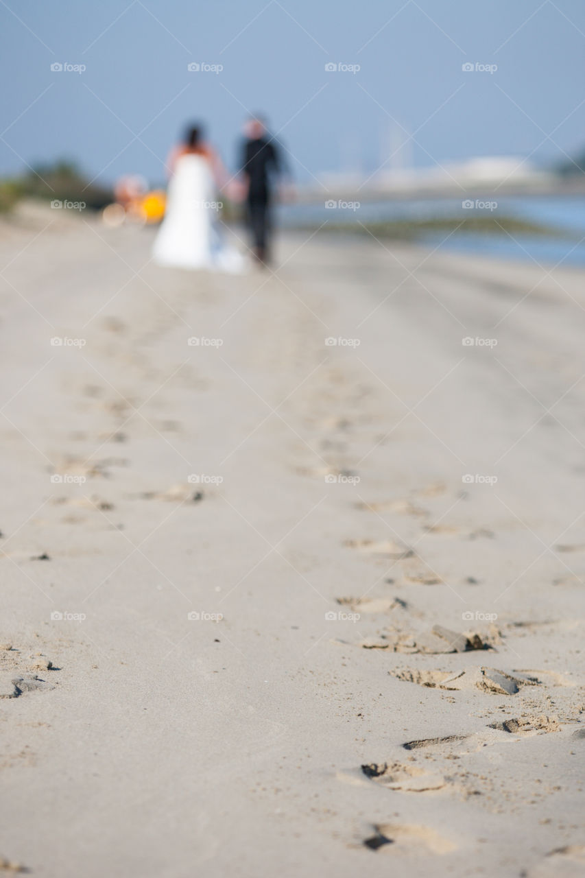 Out of focus newly wed couple walking on the beach in the distance showing their footsteps in  focus