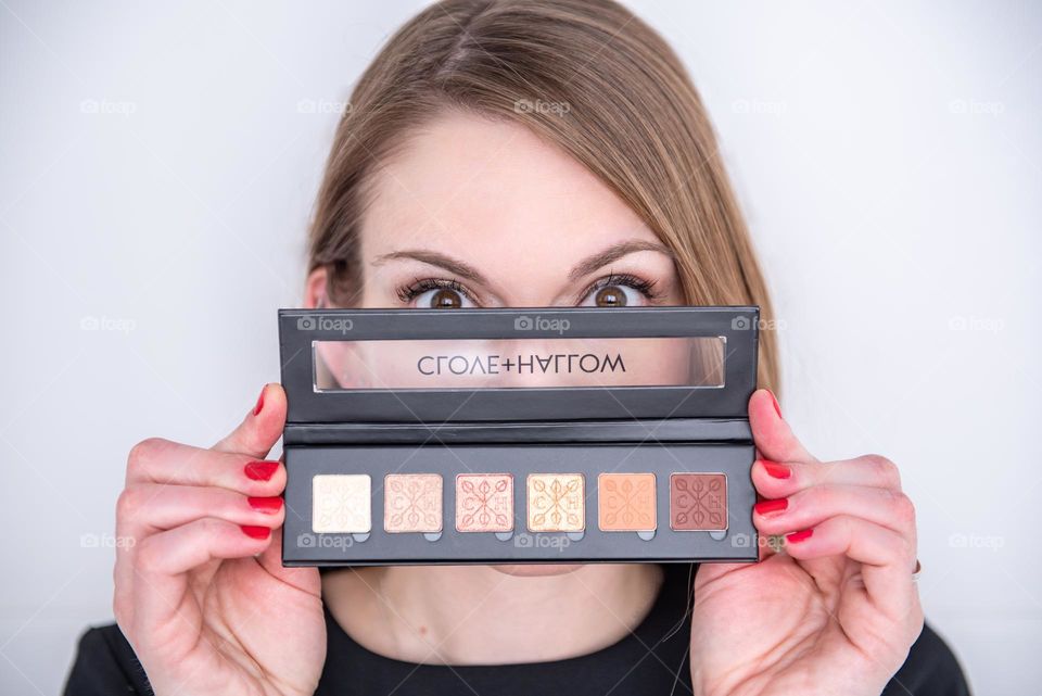 Woman playfully holding an eye shadow palette up to her face 