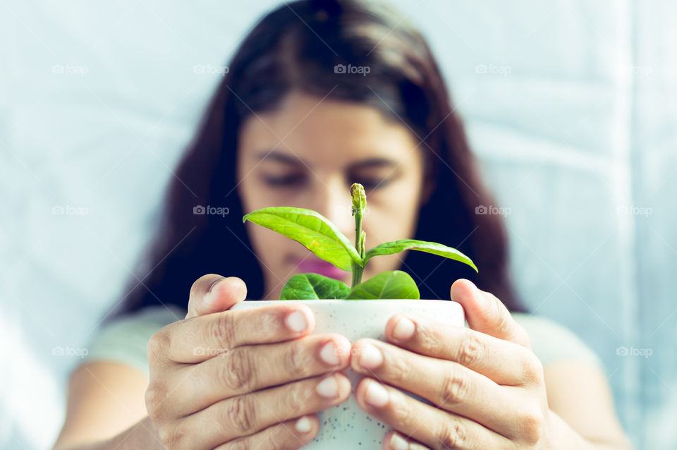 Girl holding green plant in white ceramic pot.