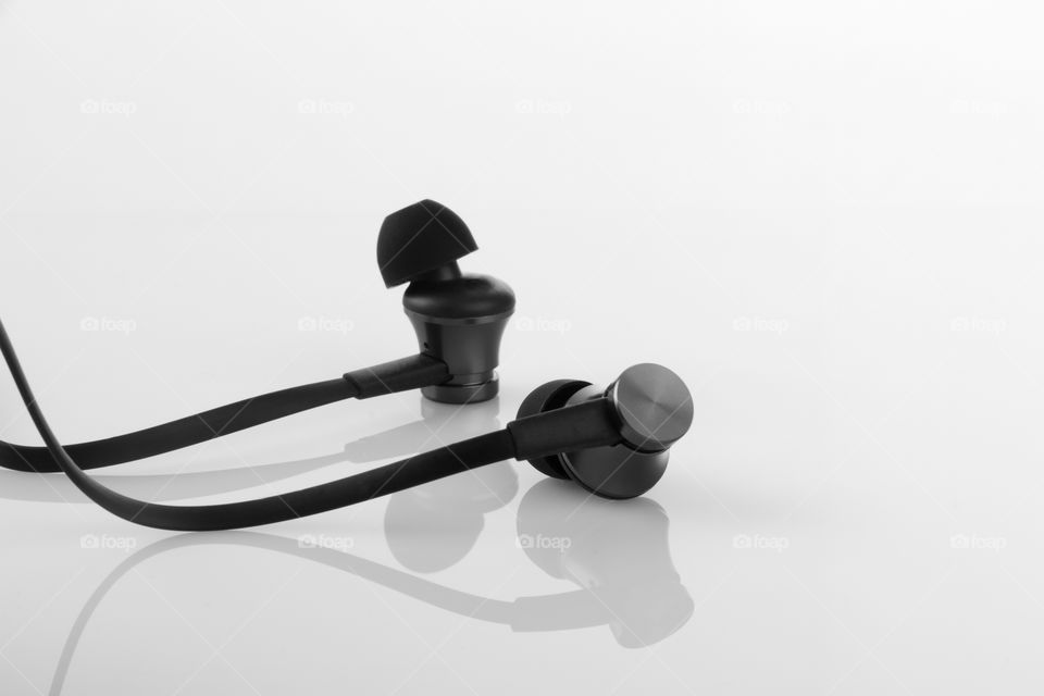 Black earphones on white reflective background