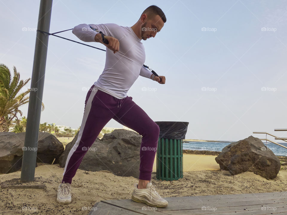 man training in the street doing various exercises with elastic band and overlooking the sea