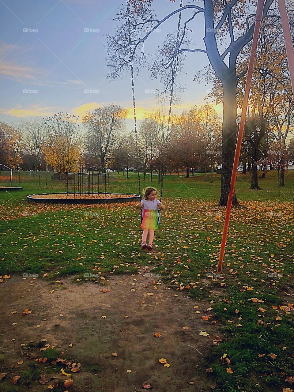 A little girl swinging in a park with a lovely sunset background 