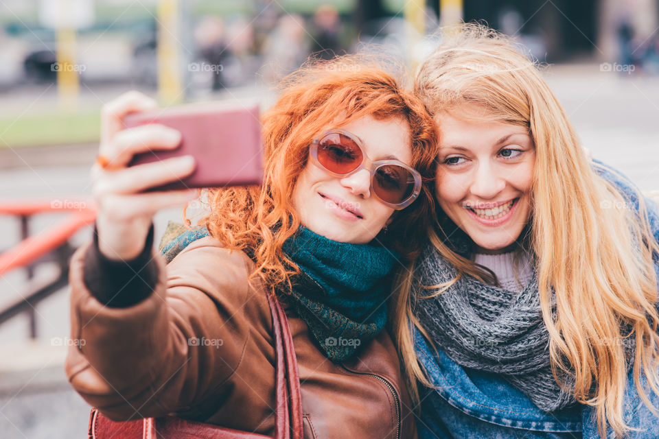 two beautiful young women friends having a video call in the street - connection, communication