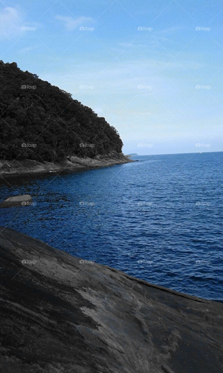 Realçando a beleza das águas azuis do oceano à beira da rocha e das matas.