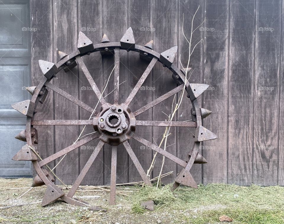 Old metal wheel leaning against an old wooden wall