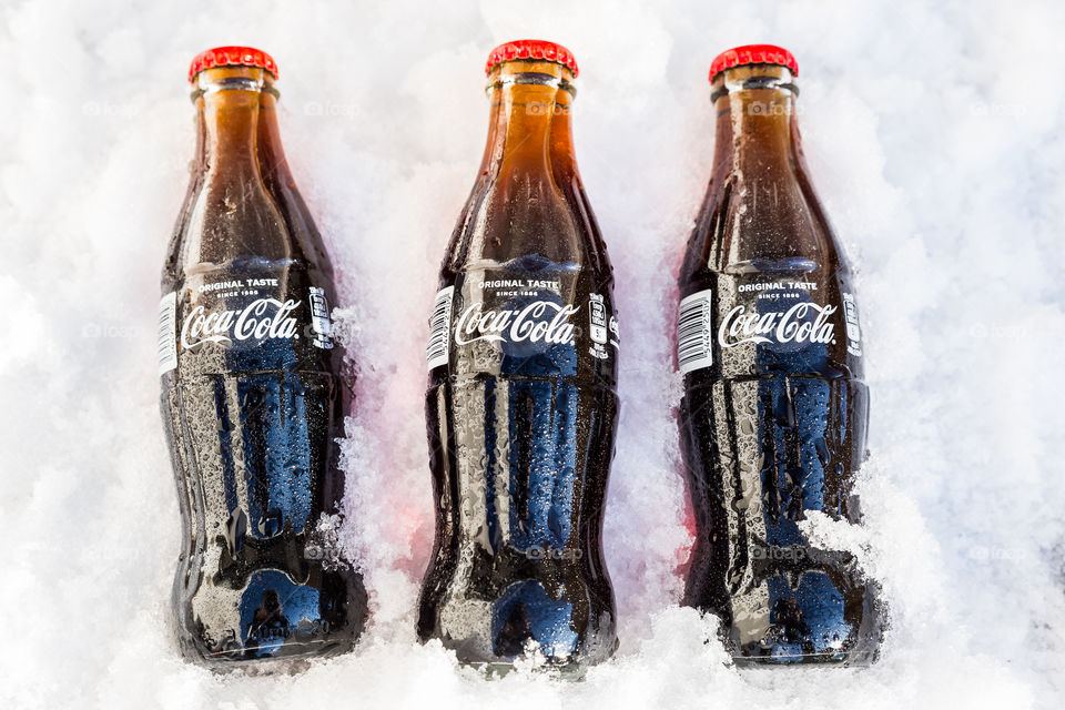 Three ice cold bottles of Coca Cola lying in the snow 