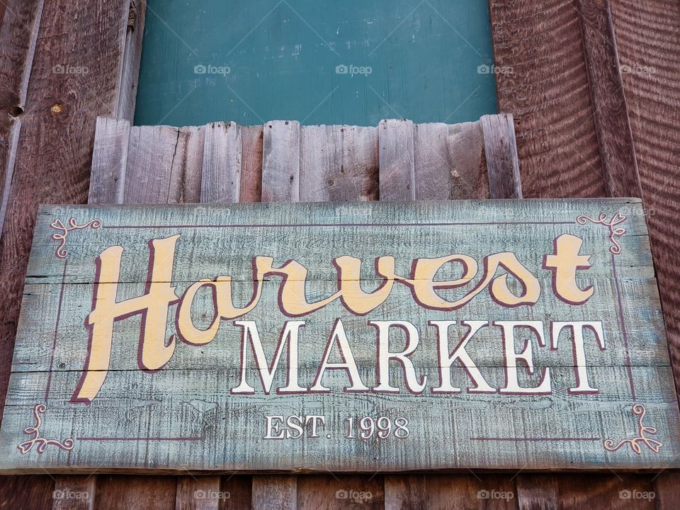 A sign for a farming harvest market made from weathered wood