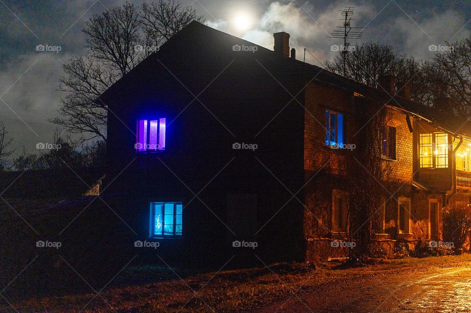 Blue, purple and warm yellow light in the windows of the house at night