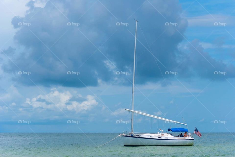 peaceful summer breeze time floating on the water with a sailboat against a stormy blue sky background