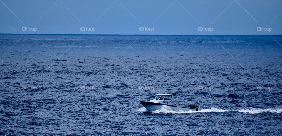 A fishing boat moving quickly along the shoreline on the east side of the Big Island of Hawaii.