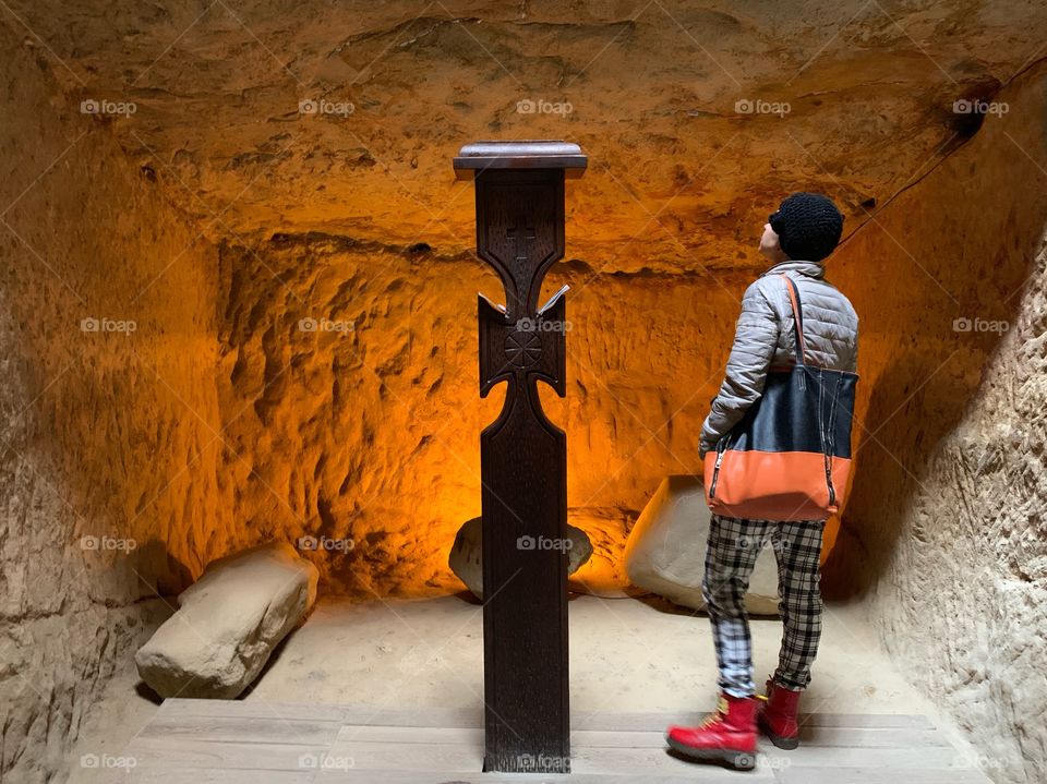 A woman looking over orange mystical lights in a cave with a cross and special vibes 