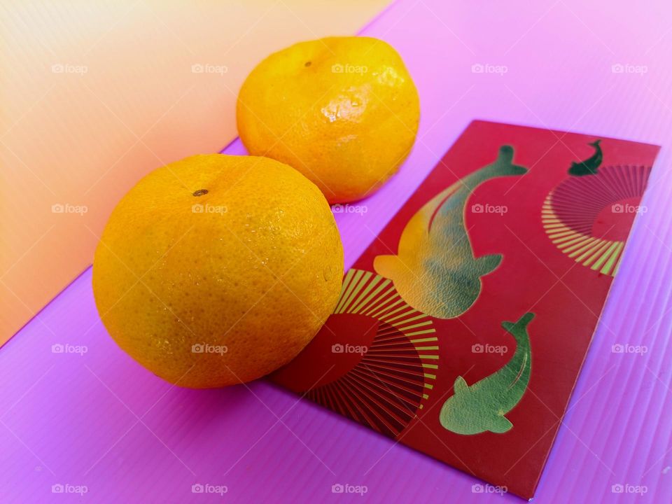 Mandarin oranges and a red packet on pink and orange background. Gifts for Chinese New Year.