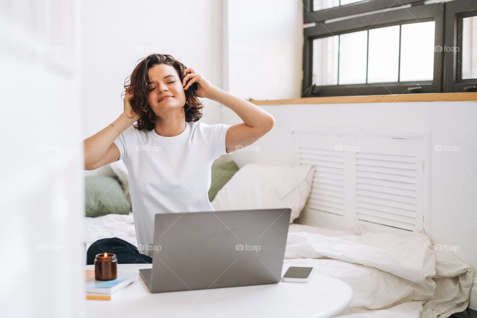 Young brunette woman with closed eyes in headphones working on laptop from home