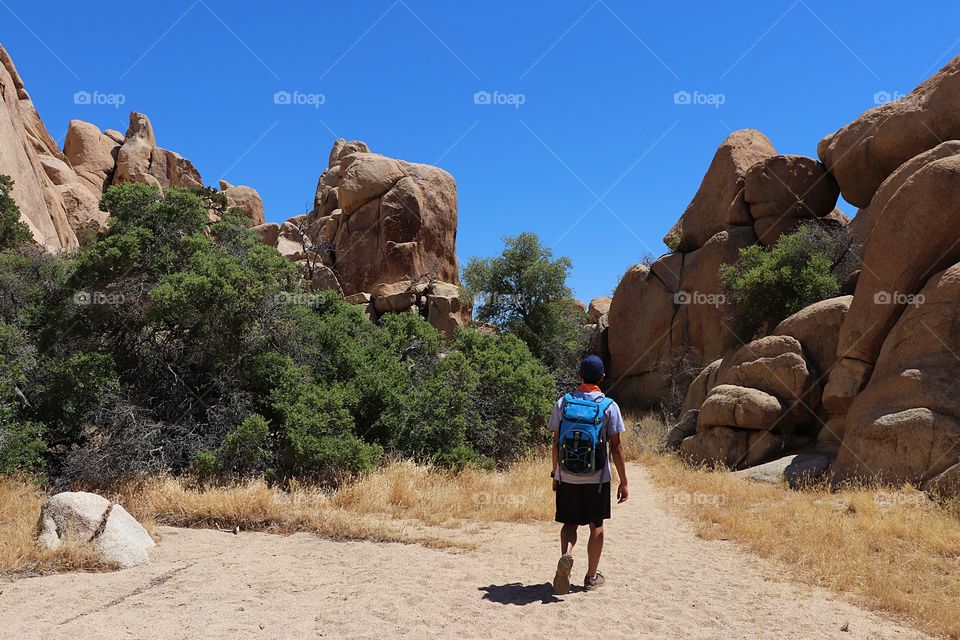 its a hot summer day, walking between two boulders on a trail at Joshua Tree National park