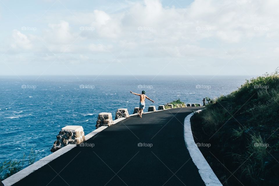 Girl runs down a road that overlooks the Pacific Ocean in Hawaii.