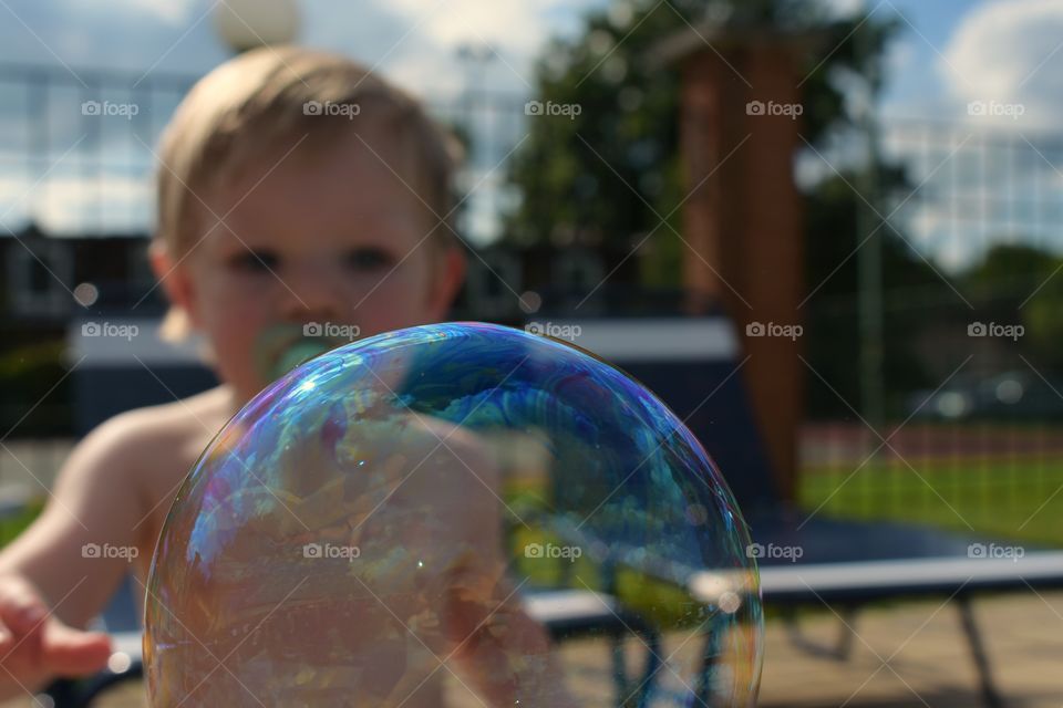 Cute baby boy playing with bubbles at pool 