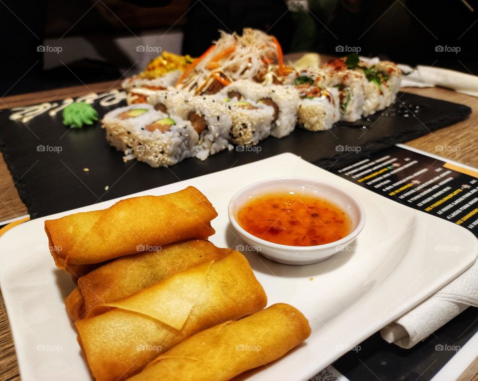 A photo in a sushi restaurant of spring rolls with dip sause and a pile of beautiful sushi bites