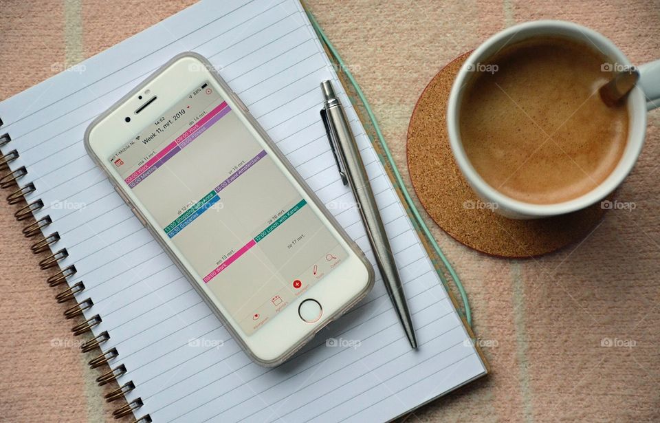 Flat lay photo of calendar on phone, lined notebook and coffee.