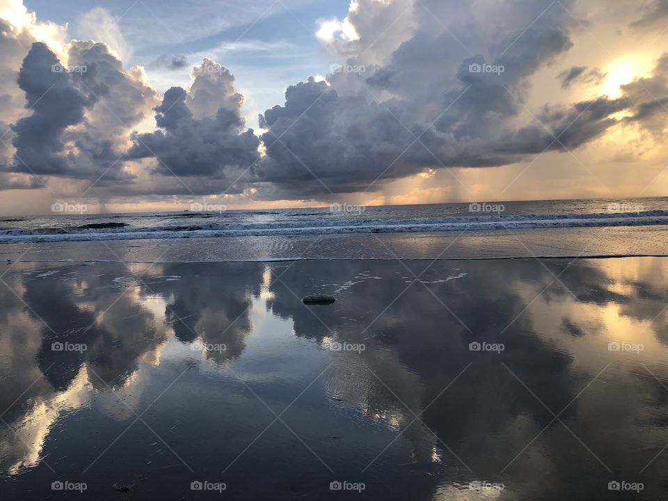 Fluffy cloud sunrise at the beach reflecting of the water