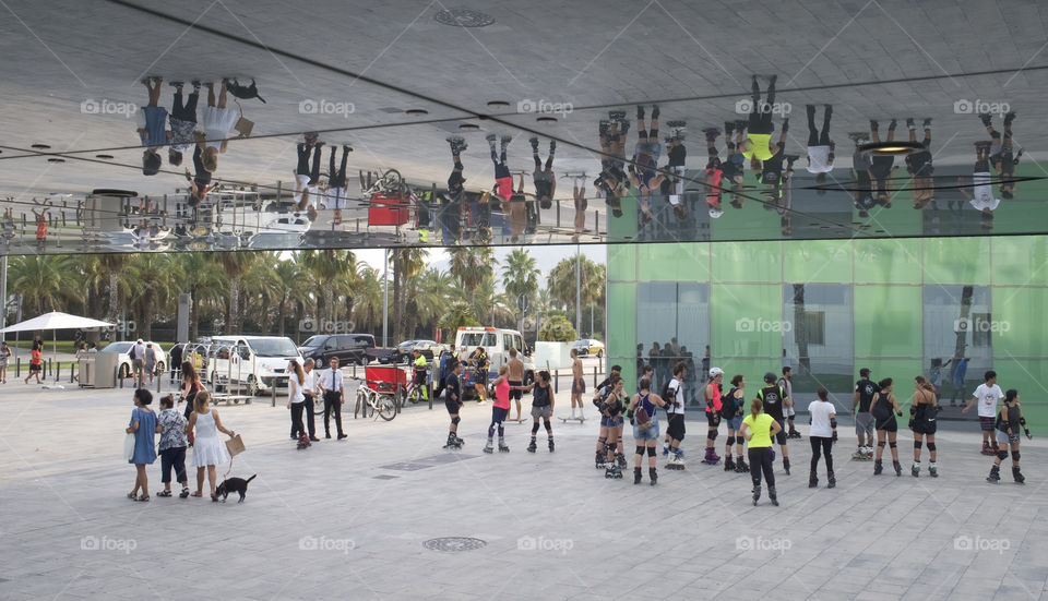 Seeing double, building glass reflection pedestrians and skaters Barceloneta Spain