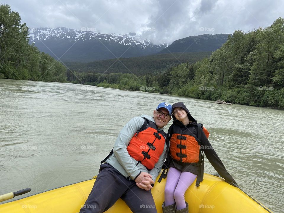 A bright pop of safety orange life jackets in a bright yellow raft floating down a river in the Alaskan Frontier 