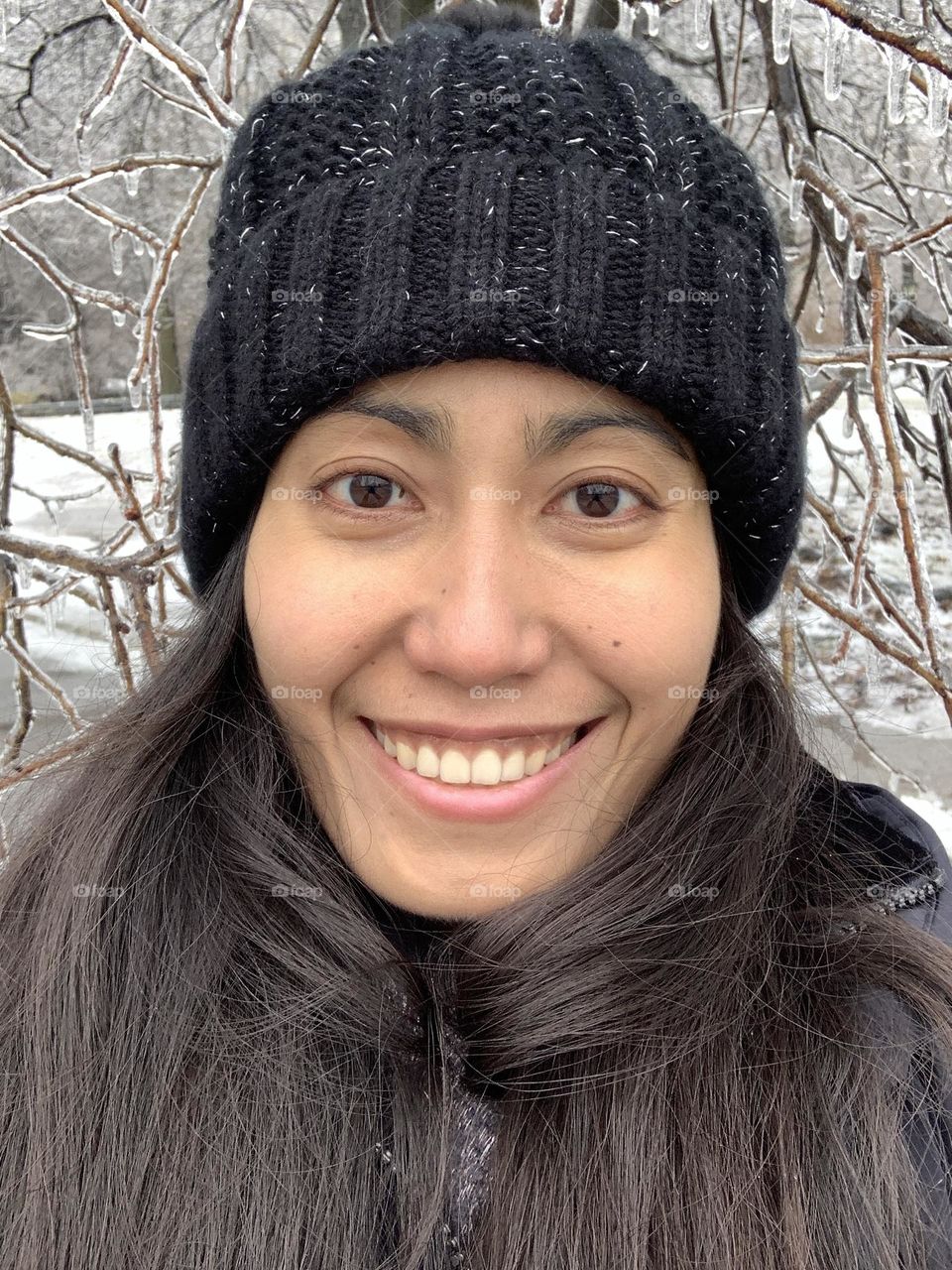 Portrait of young woman, no make up with icicles backdrop. Smiling mood and wearing bonnet in winter season.